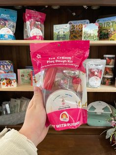 a person holding up a pink package in front of a shelf full of children's toys