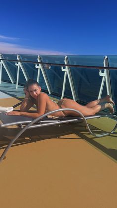 a woman laying on top of a metal chaise lounge chair next to the ocean