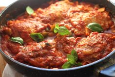 a pan filled with meat covered in sauce and garnished with fresh basil leaves