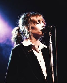 a woman singing into a microphone in front of purple and blue lights at a concert