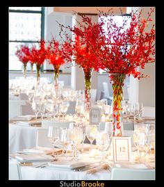 there are many vases with red flowers in them on the tables at this wedding reception