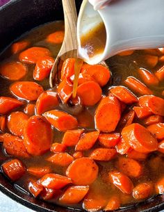 someone is stirring carrots in a pot with gravy