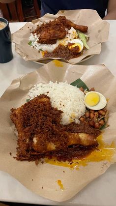 two plates filled with rice, meat and eggs on top of paper wrappers next to a cup of coffee