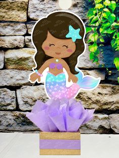 a little mermaid cutout sitting on top of a purple box with flowers in it