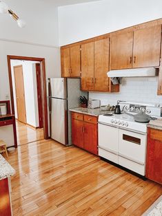 a kitchen with wooden cabinets and white appliances in it's center island area, along with hardwood flooring