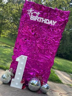 a purple birthday sign sitting on top of a cement slab next to some silver balls