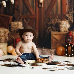 a baby wearing a cowboy hat sitting on the floor with food in front of him