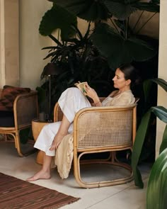 a woman sitting in a wicker chair next to a potted plant and rug