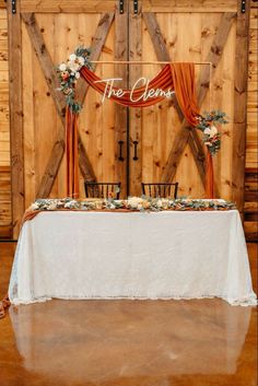 the table is set up for an event with white linens and orange drapes