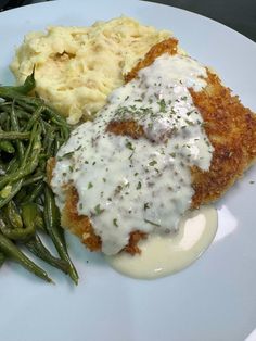 a white plate topped with meat, mashed potatoes and green beans next to gravy