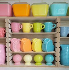 a shelf filled with lots of different colored cups and vases on top of wooden shelves