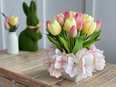 a vase filled with flowers on top of a wooden table next to a bunny statue