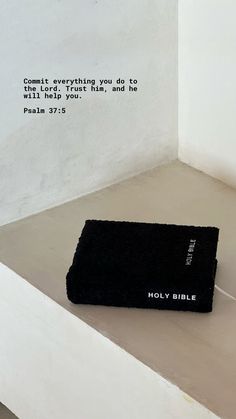 a black bible laying on top of a white table next to a wall with the words, commit everything you do