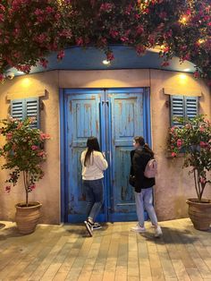 two women standing in front of a blue door with pink flowers growing on the outside