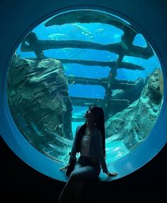 a woman sitting in front of an aquarium looking at the water