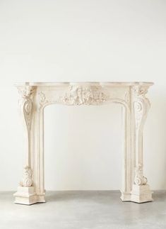 a white marble fireplace mantel with carvings on the top and sides, in an empty room