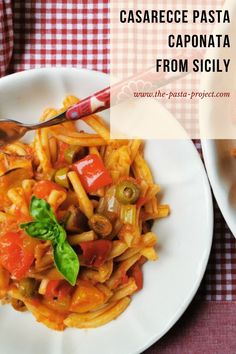 pasta with tomatoes, peppers and olives on a white plate next to a red checkered tablecloth