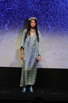 a woman standing on a stage in front of a projection screen wearing a dress and headdress