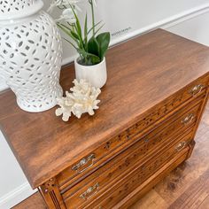 two white vases sitting on top of a wooden dresser next to a flower pot