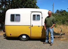 a man standing next to an old yellow and white trailer