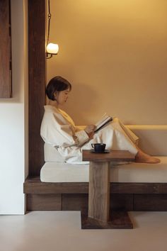 a woman is sitting on a bench reading a book and drinking a cup of coffee