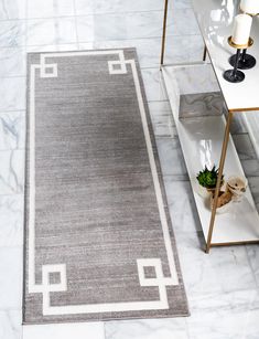 a gray rug with white trim on the floor in front of a mirror and side table