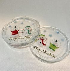 two glass coasters with snowmen on them and merry christmas written on the lids