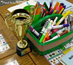 a cup filled with markers and crayons on top of a table next to a trophy