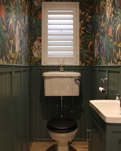 a toilet and sink in a room with wallpapered walls, green paneling and wooden floors