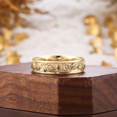 a gold wedding band with green stones on top of a wooden box in front of a wall