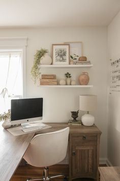 a desk with a computer on top of it next to a wall mounted shelf filled with pictures