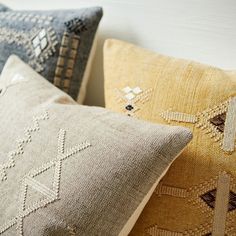 three decorative pillows are lined up against a white wall, one is blue and the other is yellow