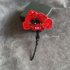 a red beaded flower brooch sitting on top of a gray cloth covered table