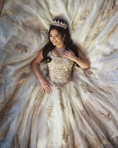 a woman wearing a tiara laying on top of a white dress with gold accents