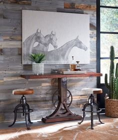 a room with two stools and a table in front of a painting on the wall