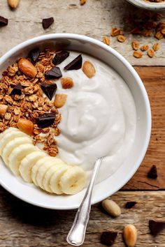 a bowl filled with yogurt, granola and nuts on top of a wooden table