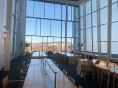 a person sitting at a table in a large room with big windows looking out on the city