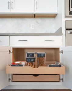 an open cabinet in a kitchen with spices and food items inside it, on the bottom shelf