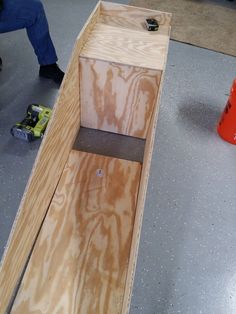 a wooden box sitting on top of a floor next to a red cone and orange cones