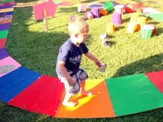 a little boy standing on top of a rainbow colored play mat in the middle of grass