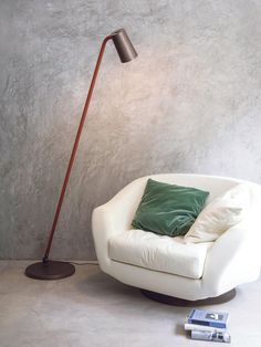 a white chair with a green pillow on it next to a floor lamp and some books