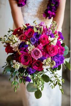 a bride holding a bouquet of purple and red flowers