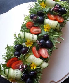 a white plate topped with cucumbers, tomatoes and black olives on top of lettuce