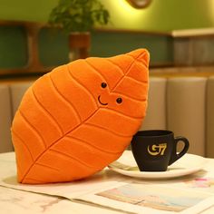 an orange leaf shaped pillow sitting on top of a table next to a coffee cup