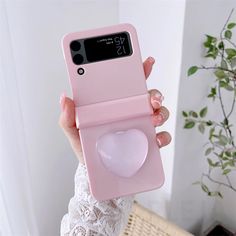 a woman holding up a pink phone case with a heart shaped object in the middle