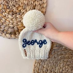 a hand holding a crocheted hat with the word george written on it