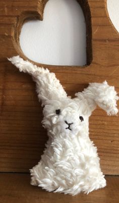 a white stuffed animal sitting in front of a heart shaped frame on a wooden surface