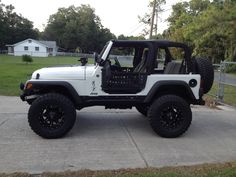 a white jeep parked on the side of a road next to a fence and trees