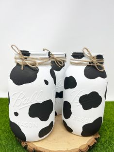 two mason jars decorated with black and white cow prints are sitting on a piece of wood