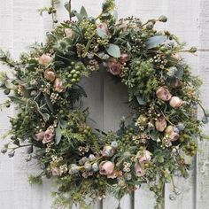 a wreath hanging on the side of a white door with flowers and greenery around it